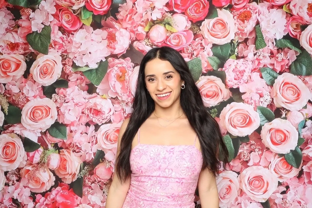 Penélope Vega Yates sonríe frente a una pared de rosas rosadas.
